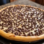 A warm and gooey Chocolate Chip Dessert Pizza on a wooden serving board, topped with melted chocolate chips and drizzled with caramel.